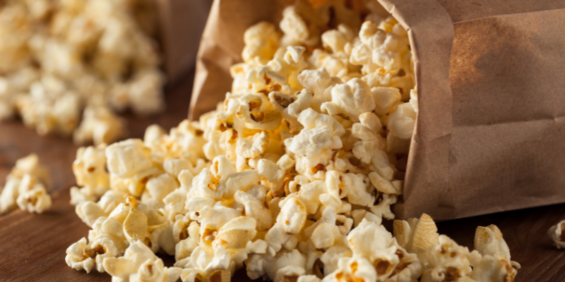 Beach Snacks - Popcorn Brown paper bag with popcorn spilling out of it.