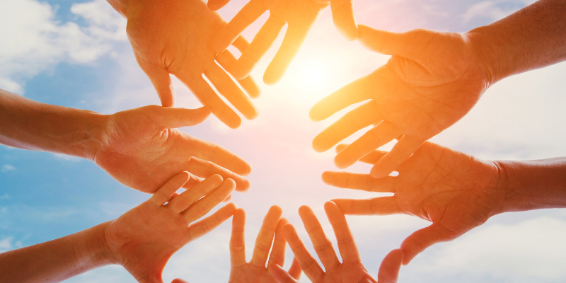 Volunteer Tourism 8 hands forming a circle against the sunshine.
