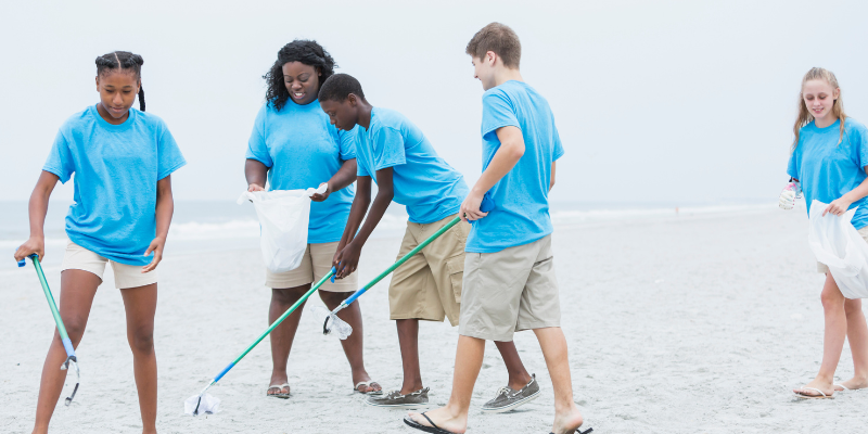 How to Volunteer on the Outer Banks Group of young people wearing blue shirts cleaning up trash on the beach.
