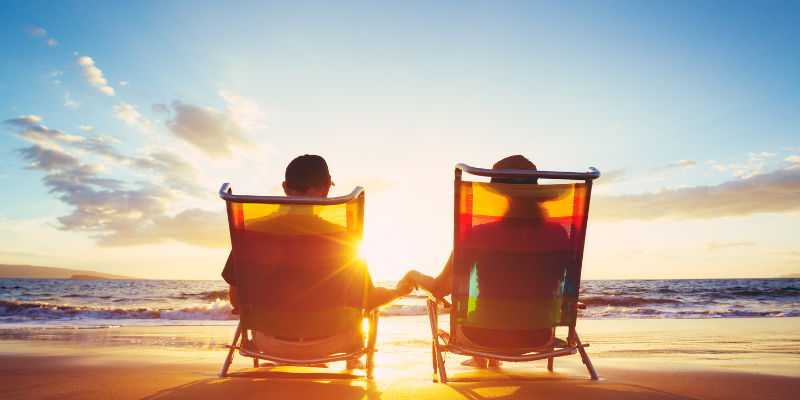 Top 10 Reasons to Visit the Outer Banks in May Couople sitting in chairs on the beach, holding hands, and watching the sunrise.