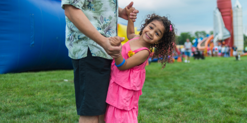 Outer Banks May Events Dad and daughter dancing outside in front of an inflatable slide.