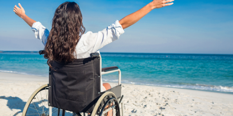 Tips for Marketing Your Accessibility Options Woman in a wheelchair at the beach with her arms raised to the sky.