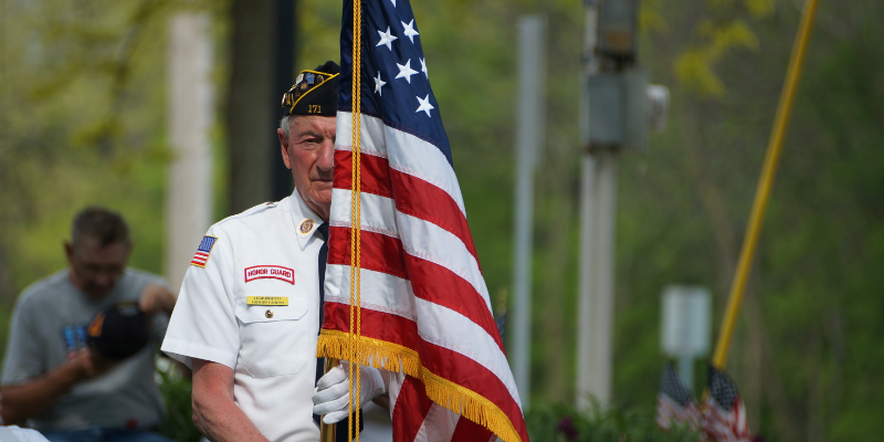Find Out More about Outer Banks Veteran Week! Honor Guard member standing behind American Flag