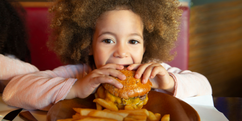 The Outer Banks is Full of Family-Friendly Dining Experiences! Young girl eating a hamburger at a restaurant.