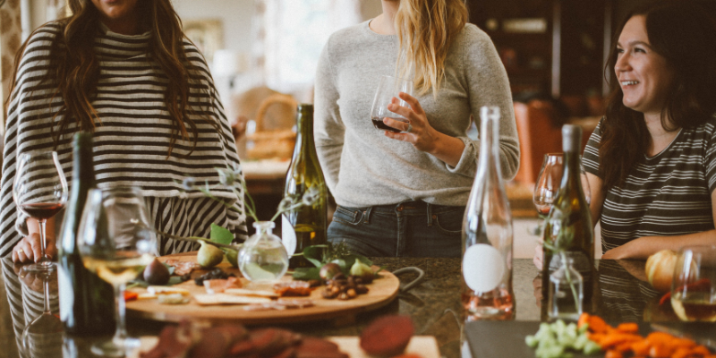 Three women talking and laughing around counter with food on it.