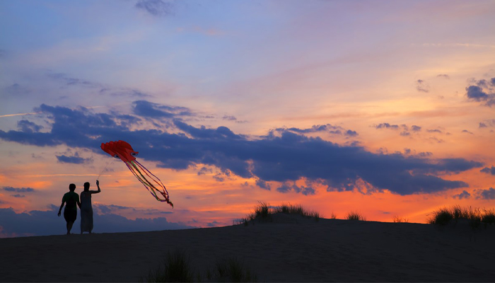 Two people flying a red kite with a colorful blue and orange sky