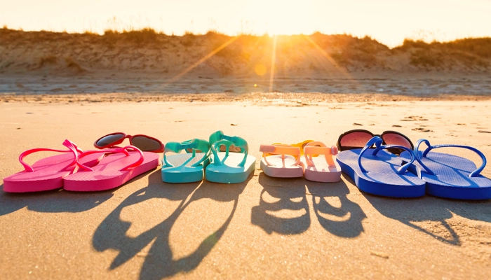 4 pairs of brightly colored flip flops and two pairs of sunglasses sitting on the sand