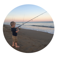 Small child holding a fishing rod looking out at the ocean