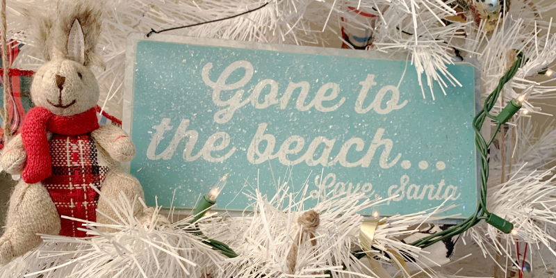 OBX Christmas Ornament OBX Christmas Ornament - Blue Christmas Ornament that says "Gone to the beach, love Santa" in white font sitting in white Christmas tree. Toy bunny with plaid stomach sitting next to it.
